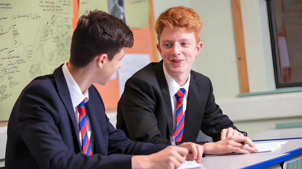 Zwei Schüler der Loughborough Grammar School unterhalten sich an einem Schreibtisch im Klassenzimmer mit Tafel im Hintergrund.