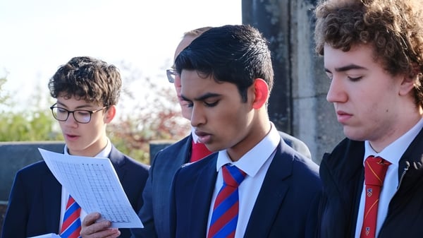 Drei Schüler der Loughborough Grammar School diskutieren gemeinsam im Freien vor einem Schulgebäude mit Bäumen im Hintergrund.