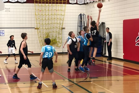 Eine Gruppe Schülerinnen und Schüler spielt Basketball auf dem Sportplatz der École secondaire publique Louis-Riel.