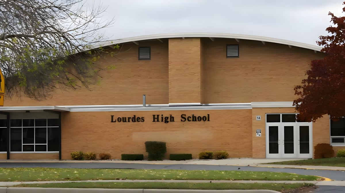 Das Backsteingebäude der Lourdes Academy ist von Bäumen und einer Grünfläche umgeben.