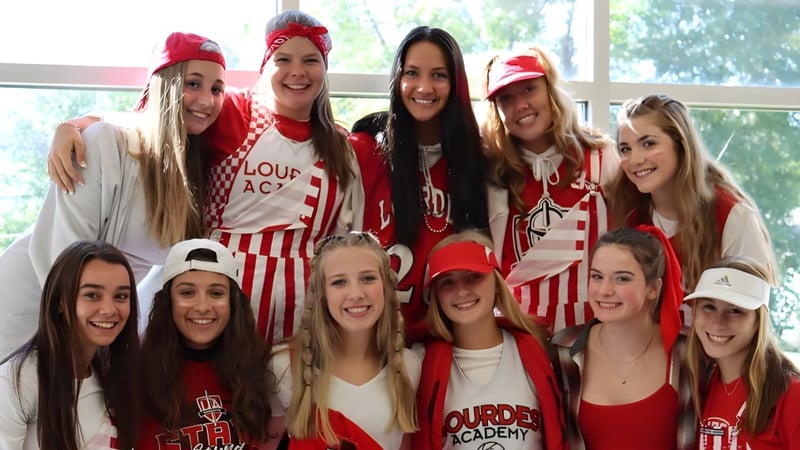 Eine Gruppe junger Schülerinnen posiert in roter und weißer Kleidung auf dem Campus der Lourdes Academy.