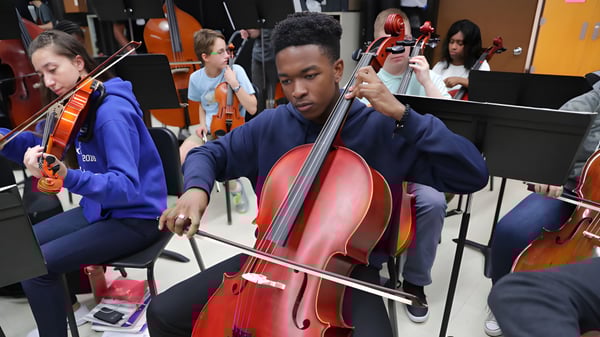Ein Schüler der Lowell Catholic High School spielt intensiv ein großes rotes Cello bei einer Musikprobe.