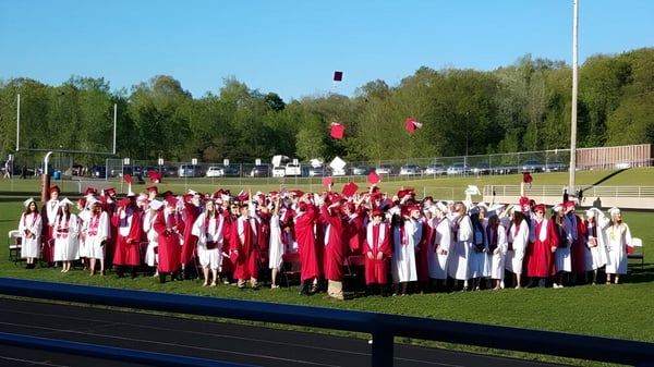 Schüler der Lowell High School versammeln sich in roten und weißen Abschlusskleidern auf dem Sportfeld für ihre Abschlussfeier.