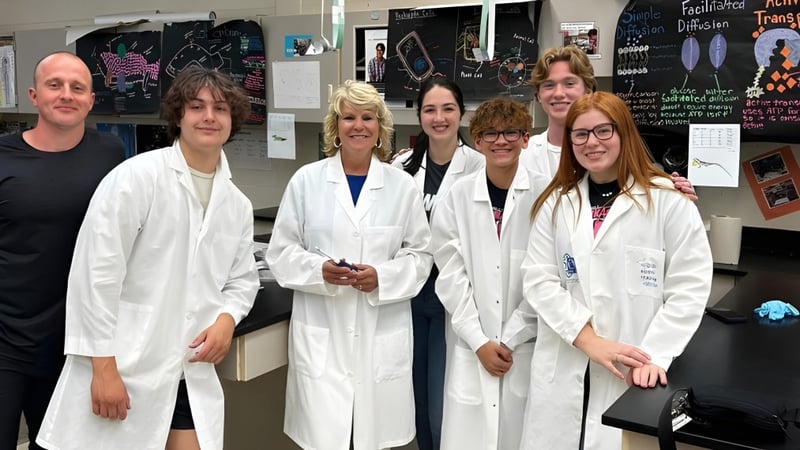 Schüler der Lowell High School stehen in weißen Laborkitteln gemeinsam in einem Klassenraum mit wissenschaftlichen Postern.