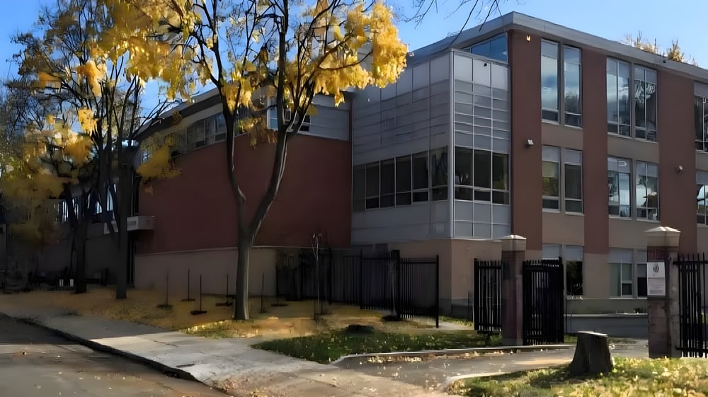 Das moderne Gebäude des Lower Canada College ist von Bäumen mit gelben Herbstblättern umgeben und zeigt einen gepflasterten Weg im Vordergrund.