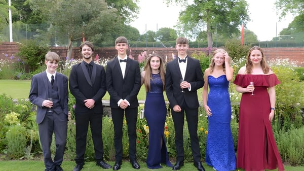 Eine Gruppe von Schülern der Lucton School in formeller Kleidung steht gemeinsam in einem Garten mit Bäumen und Grünflächen.