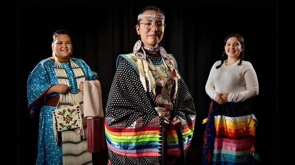 Drei Schüler der Luther College High School tragen traditionelle Native American Kleidung mit farbenfrohen Mustern und Kopfschmuck.
