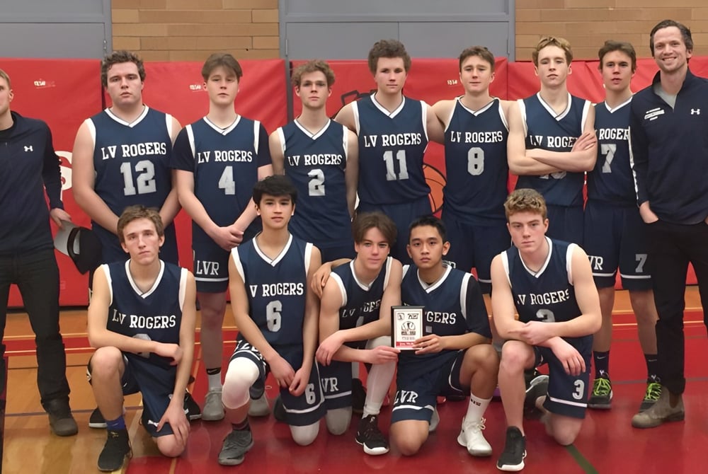 Eine Gruppe von Schülern der L.V. Rogers Secondary School posiert gemeinsam auf einem Basketballfeld mit rotem Hintergrund.