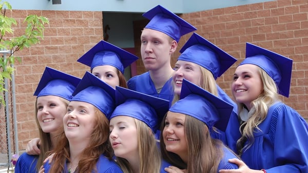 Eine Gruppe lächelnder Absolventinnen und Absolventen der L.V. Rogers Secondary School steht vor einem Backsteingebäude.