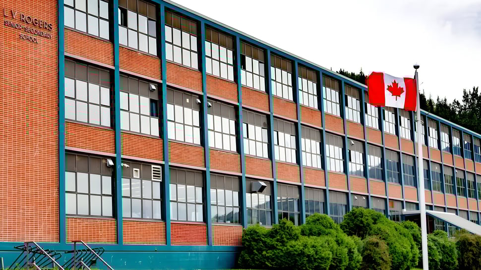 Das Backsteingebäude der L.V. Rogers Secondary School mit großen Fenstern und einer kanadischen Flagge vor Bäumen.