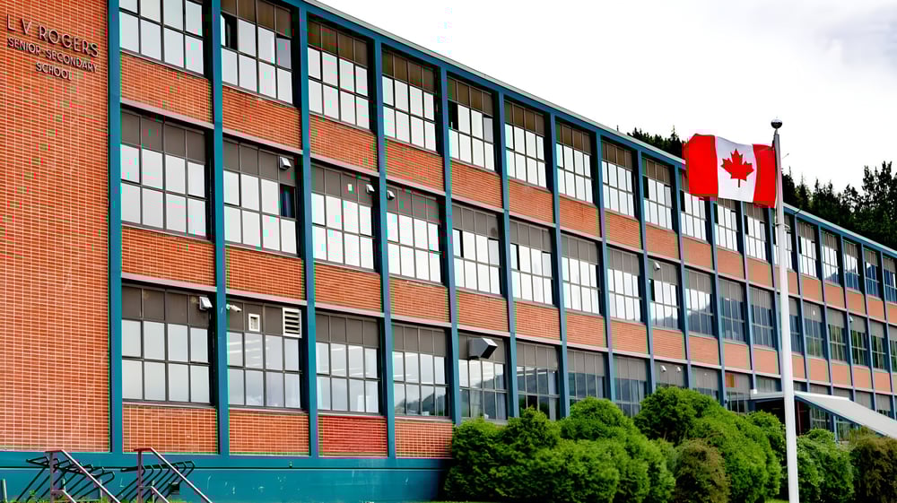 Das Backsteingebäude der L.V. Rogers Secondary School mit großen Fenstern und einer kanadischen Flagge vor Bäumen.