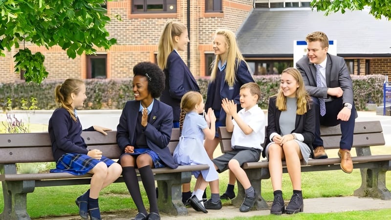 Eine Gruppe von Schülerinnen und Schülern sitzt auf einer Bank vor einem Backsteingebäude auf dem Campus der LVS Ascot.