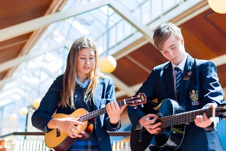 Zwei Schülerinnen der LVS Ascot spielen in einem hellen Raum mit großen Fenstern Gitarre.