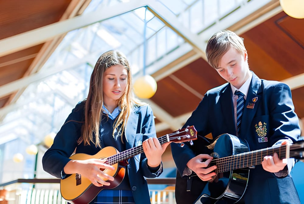 Zwei Schülerinnen der LVS Ascot spielen in einem hellen Raum mit großen Fenstern Gitarre.