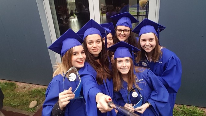 Eine Gruppe junger Frauen in blauen Abschlussroben steht gemeinsam vor einem Gebäude auf dem Campus des Lycée Charles Péguy.
