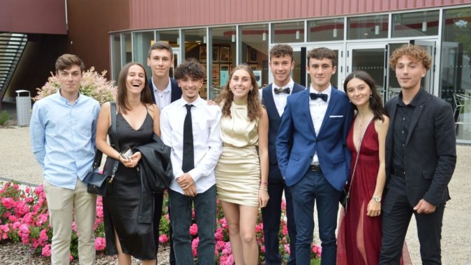 Eine Gruppe von gut gekleideten Personen steht gemeinsam vor dem pinkfarbenen Gebäude des Lycée Charles Péguy.