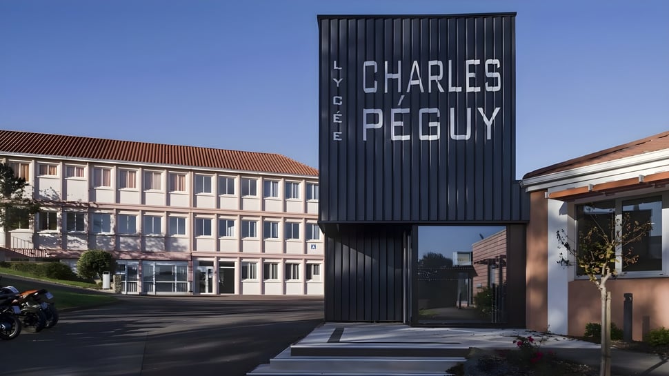 Große schwarze Struktur mit dem Schriftzug Charles Péguy vor modernen Gebäuden auf dem Campus des Lycée Charles Péguy.