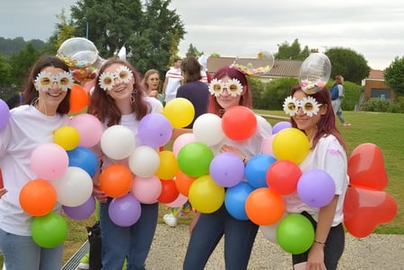 Eine Gruppe Schülerinnen des Lycée Charles Péguy mit bunten Masken hält verschiedene Luftballons im Freien auf einer Wiese.