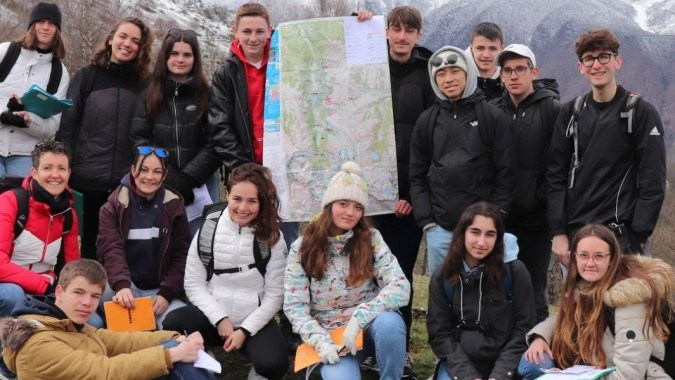 Schüler des Lycée Charles Péguy versammeln sich draußen mit verschneiten Bergen im Hintergrund.
