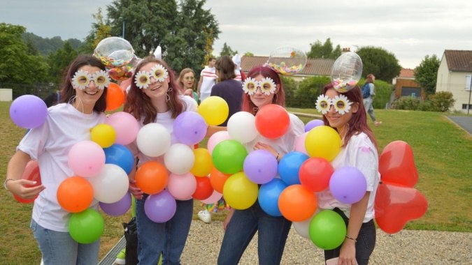 Schülerinnen des Lycée Charles Péguy stehen draußen mit bunten Luftballons und tragen spielerische Gesichtsmasken vor ländlicher Kulisse.