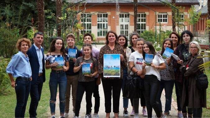Schüler des Lycée Gabriel Fauré stehen vor einem Gebäude mit buntem Wandgemälde und zeigen eine Stadtlandschaft als Kunstwerk.