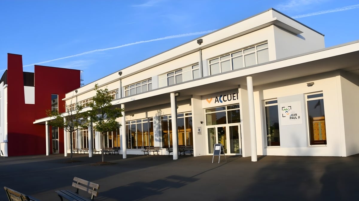 Das moderne Gebäude des Lycée Immaculée Jean Paul II mit beigen und roten Akzenten steht vor einem klaren Himmel.