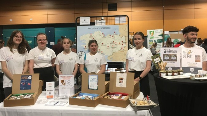 Schüler des Lycée Immaculée Jean Paul II stehen hinter einem Tisch mit Produkten und Informationsmaterialien.