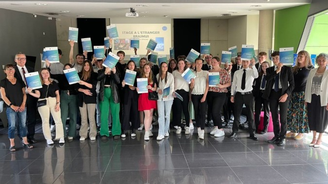 Eine Gruppe von Schülerinnen und Schülern hält im Raum mit grüner Wand und Banner bei Lycée Immaculée Jean Paul II verschiedene Schilder hoch.