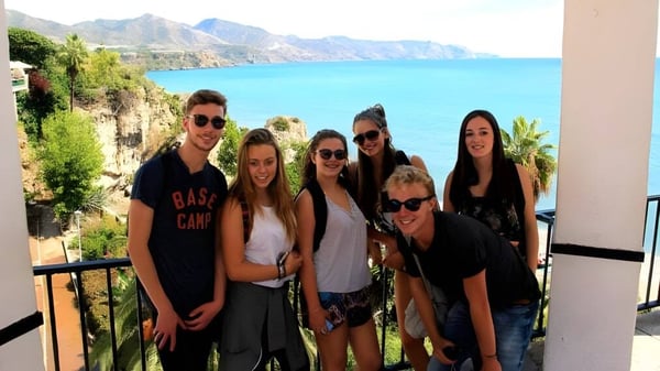 Eine Gruppe Schülerinnen und Schüler des Lycée Jean Brito posiert vor einer Küstenlandschaft mit Bergen und türkisfarbenem Meer.