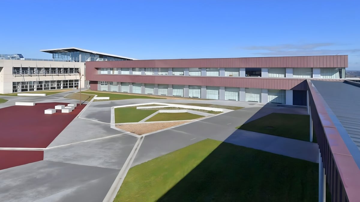 Das moderne Hauptgebäude des Lycée Jean Brito mit einem farbenfrohen, geometrisch gemusterten Innenhof bei klarem Himmel.