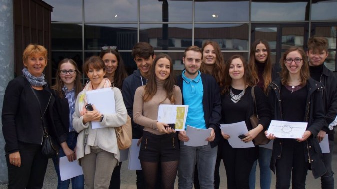 Eine Gruppe Schüler steht vor dem Glasgebäude des Lycée Jean Brito und hält Papiere in der Hand.
