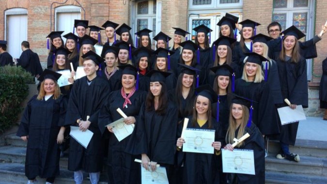 Eine Gruppe von Absolventinnen und Absolventen des Lycée Notre Dame de Bon Secours steht vor einem Backsteingebäude mit ihren Diplomen.