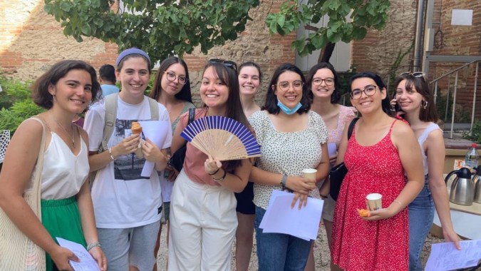 Eine Gruppe junger Frauen mit Fächern steht auf dem Außengelände des Lycée Notre Dame de Bon Secours vor einem Backsteingebäude.