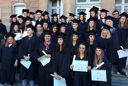 Eine Gruppe von Absolventen des Lycée Notre Dame de Bon Secours steht vor einem Backsteingebäude und hält ihre Diplome.