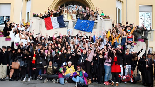 Eine Gruppe Schüler vor dem Lycée Polyvalent Philippine Duschenes zeigt polnische und EU-Flaggen vor einem Gebäude mit Bogen.