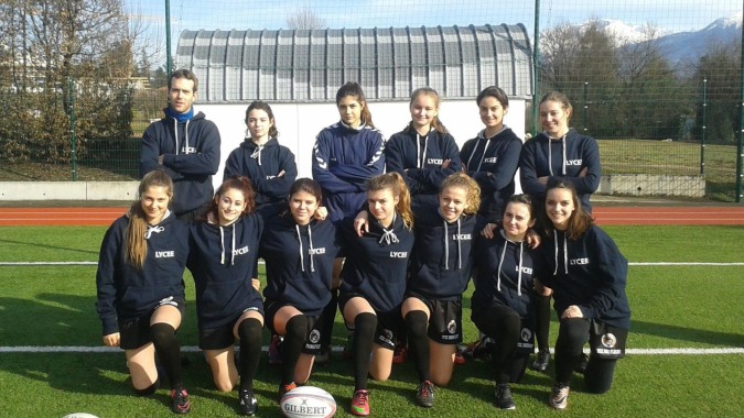 Eine Gruppe junger Fußballspielerinnen steht auf dem Sportplatz des Lycée Polyvalent Philippine Duschenes vor einem großen Gebäude.