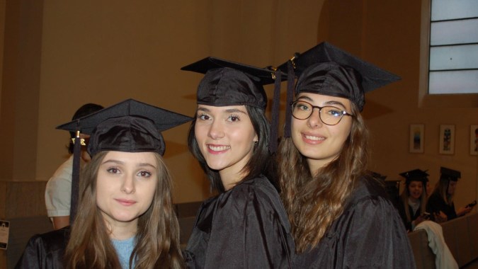 Drei Schülerinnen der Lycée Polyvalent Philippine Duschenes posieren gemeinsam in Abschlusskleidung in der Schule.