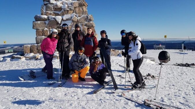 Schüler des Lycée Saint Antoine stehen vor einer großen Steinstruktur am schneebedeckten Berghang bei klarem Himmel.