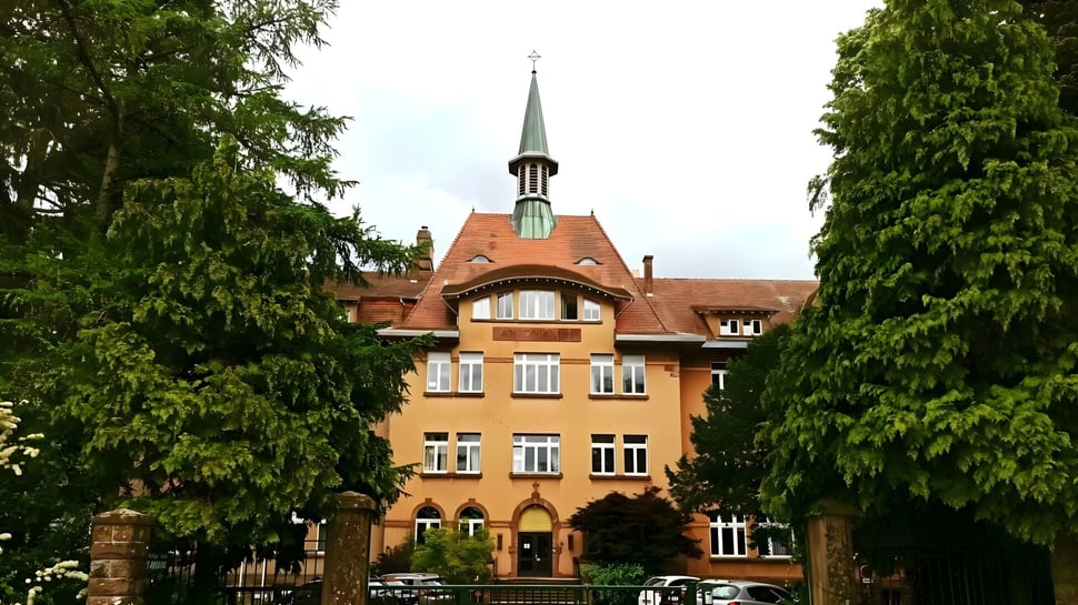 Das Gebäude des Lycée Saint Antoine mit einem auffälligen Turm steht umgeben von grünen Bäumen.