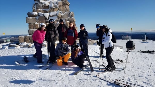 Eine Gruppe von Schülerinnen und Schülern des Lycée Saint Antoine steht in Winterkleidung vor einer Steinstruktur auf einem schneebedeckten Berghang.
