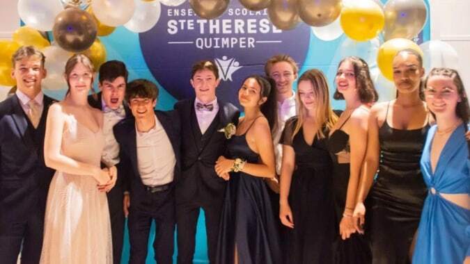 Eine Gruppe von Personen in formeller Kleidung posiert vor einem Hintergrund mit dem Schriftzug Quimper auf dem Campus des Lycée Sainte Thérèse.