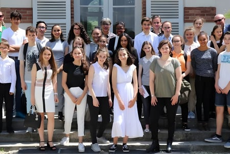 Eine Gruppe Schülerinnen und Schüler steht vor einem Gebäude des Lycée Sainte Thérèse mit Fensterläden und Blumentöpfen.