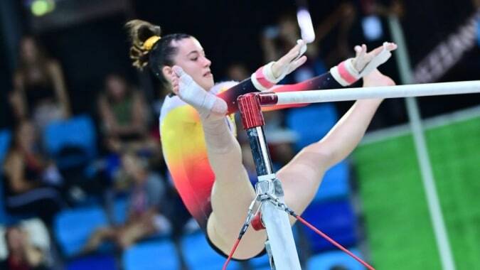 Eine Turnerin des Lycée St Elme zeigt eine Übung am unebenen Barren vor Publikum.