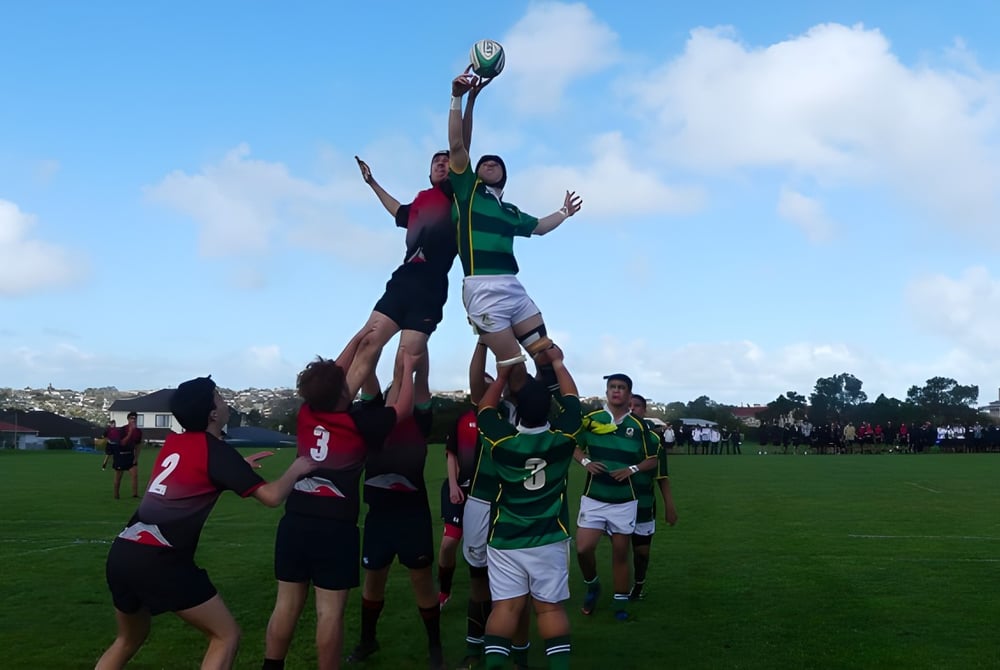 Eine Gruppe Schüler spielt Rugby auf dem Sportfeld des Lynfield College unter blauem Himmel mit Wolken.