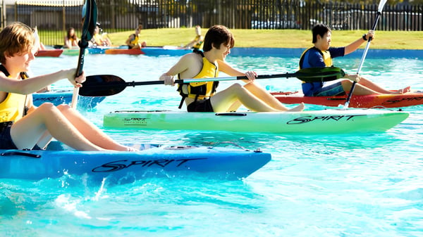 Schüler der Lynwood Senior High School bei Wassersportaktivitäten mit bunten Kajaks in einem Außenpool.