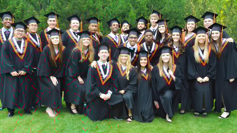Eine Gruppe von Absolventinnen und Absolventen der M.E. LaZerte Composite High School steht auf einem Rasen vor grüner Landschaft in akademischer Kleidung.