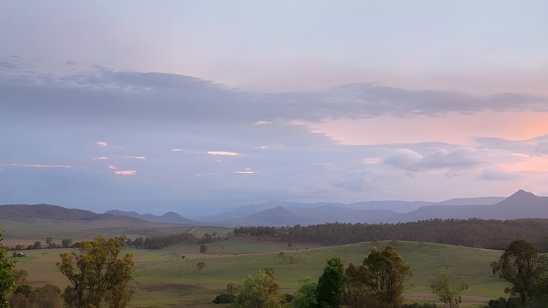Landschaft mit Hügeln, Wäldern und Bergen bei Sonnenuntergang, ohne direkten Bezug zur Mabel Park State High School.