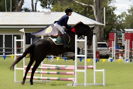 Eine Schülerin der Mabel Park State High School reitet über einen Sprung auf einem Pferd auf einem grasbewachsenen Feld.