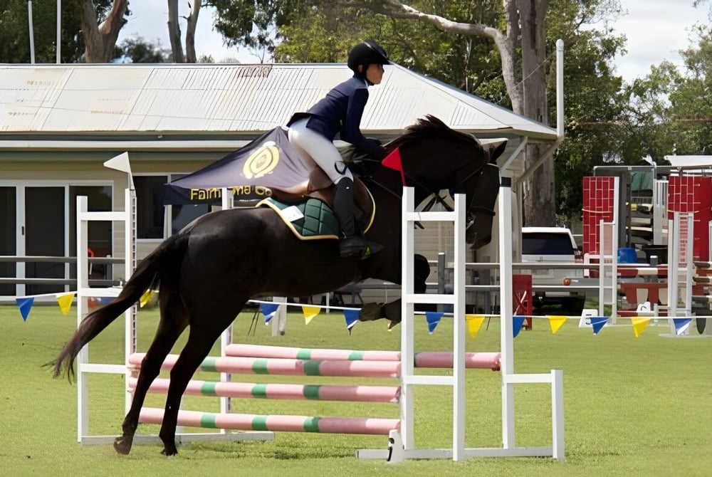 Eine Schülerin der Mabel Park State High School reitet über einen Sprung auf einem Pferd auf einem grasbewachsenen Feld.