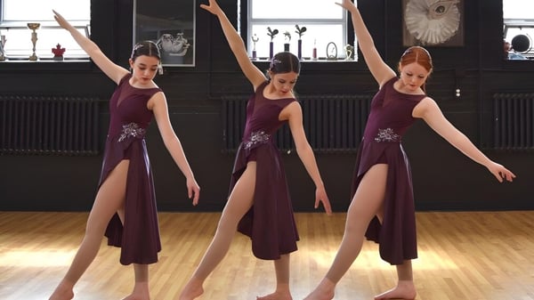 Drei Schülerinnen in burgundroten Kleidern der Macdonald High School führen eine Tanzroutine in einem Studio auf.